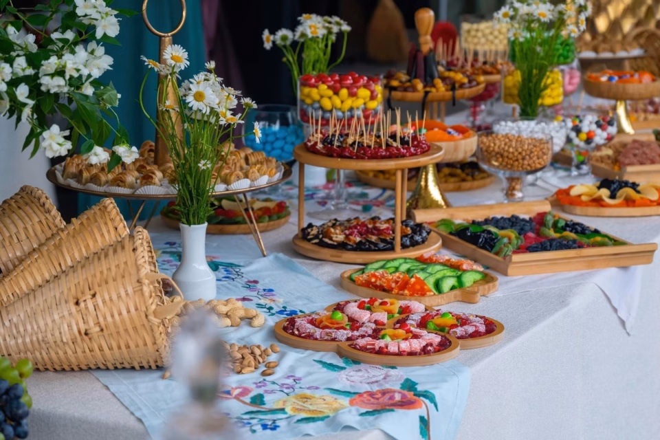 მრავალფეროვანი საქორწილო ფურშეტის მაგიდა, გაწყობილი სხვადასხვა სახის ტკბილეულით, ხილით და დეკორატიული ყვავილებით.